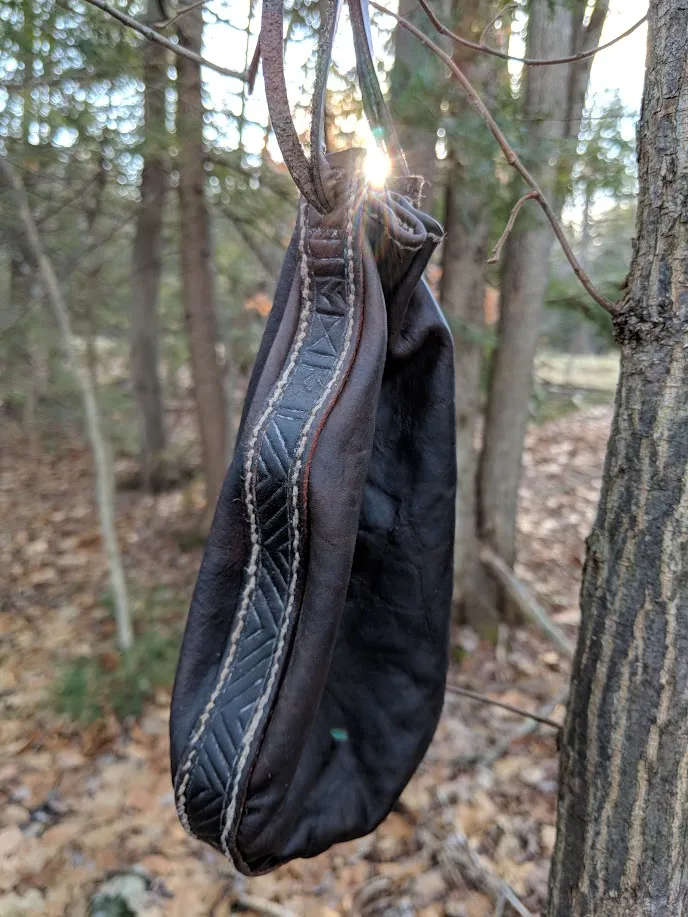 A dark leather purse hanging from a tree in autumn woods