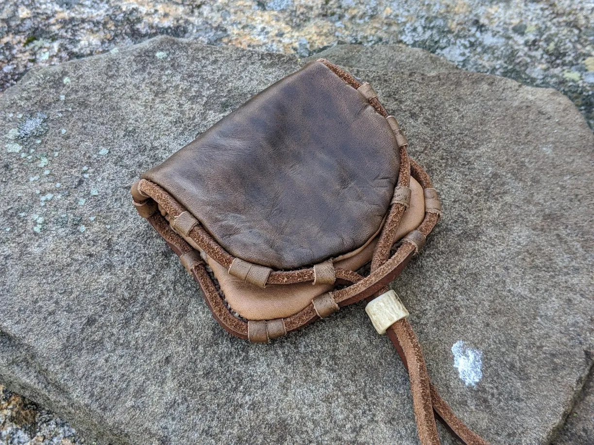 A brown leather wallet with a toggle, on grey stone