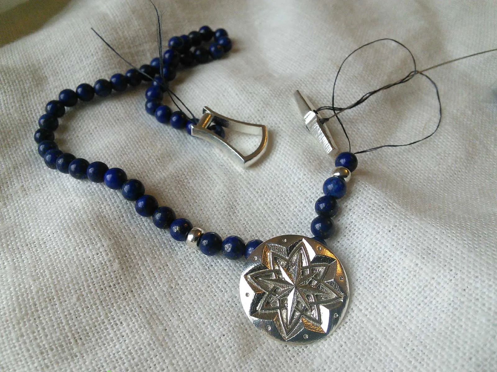 A silver star-flower pendant on a cord of lapis beads, on linen